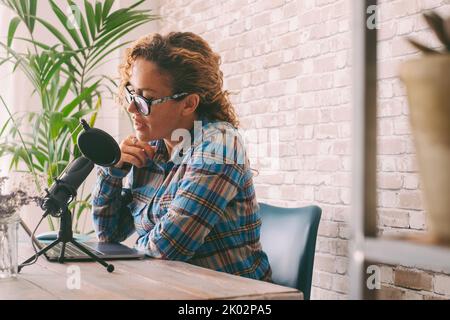Content Creator Erwachsene Frau Aufnahme eines Podcast Interview mit Mikrofon und Laptop sitzen am Schreibtisch. Home Office-Arbeitsplatz und intelligentes Arbeiten moderner Lebensstil. Online Radio Computer Job Stockfoto