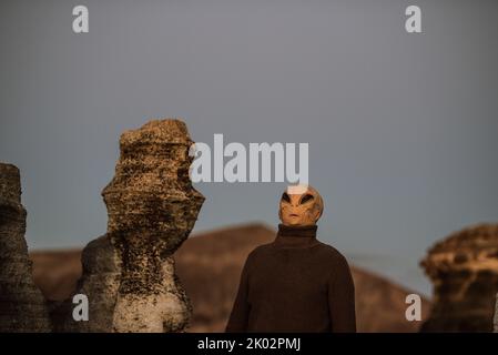 Alien-ufo-Porträt mit Mondlandschaft im Hintergrund. Stehende außerirdische Menschen auf dem Planeten Erde an einem landschaftlich schönen Ort im Freien. Konzept der Invasion oder Vielfalt. Menschen und Menschen Stockfoto