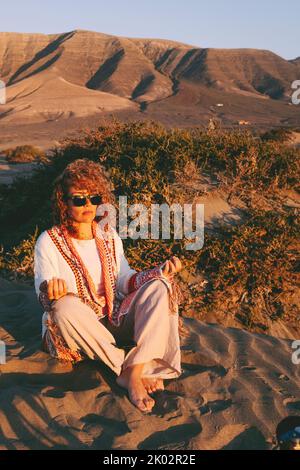 Alternative Lifestyle-Menschen mit attraktiven Frau, die Meditation Freizeit im Freien sitzen auf dem Sand in Lotos Yoga-Position. Innere Balance und Positivität. Weibliche Menschen, die Achtsamkeitsübungen machen Stockfoto