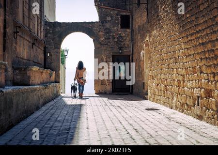 Italien, Toskana, Pienza, Frau mit Hund in der Gasse Stockfoto