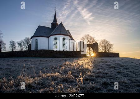 Deutschland, Hessen, Mittelhessen, Limburg-Weilburg, Taunus, Hintertaunus, Goldener Grund, Bad Camberg, Kreuzkapelle mit ersten Sonnenstrahlen am frostigen Wintermorgen ausgesetzt Stockfoto