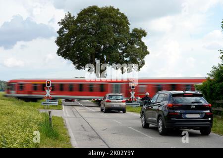 Deutschland, Bayern, Landkreis Altötting, Landstraße, Bahnübergang mit Schranken, Nahverkehrszug durchfahren, Waggons warten Stockfoto