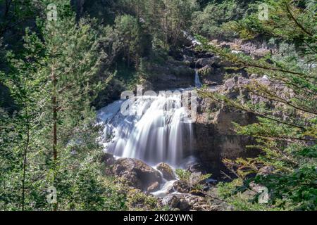 Eine Langzeitaufnahme eines kleinen Wasserfalls, der bei Tageslicht von üppigen Wäldern umgeben ist Stockfoto