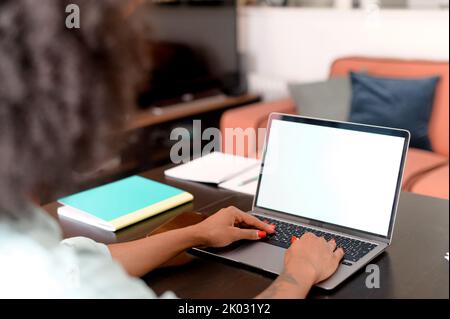 Studentin mit Laptop für Webinare, Vorträge, sitzt am Schreibtisch im Heimbüro und macht sich Notizen, östliche Frau nimmt an einem Online-Bildungskurs Teil, erforscht Themen, Kopierraum Stockfoto