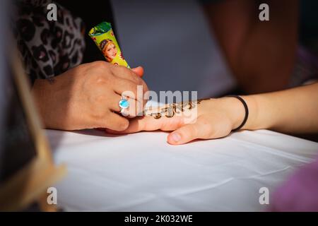 Nahaufnahme eines Mehndi-Meisters, der Henna-Tattoo auf weiblicher Hand zeichnet Stockfoto