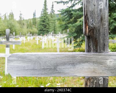 Altes Holz. Kreuz aus der Nähe mit unfokussierten weißen Kreuzen des Friedhofs in dawson City, Yukon Territory, Kanada. Stockfoto