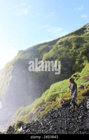 Eine vertikale Aufnahme einer Frau, die auf einer bergigen Formation in Island unterwegs ist Stockfoto