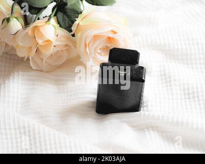 Eine Flasche Parfüm mit einer weißen Rose auf einem weißen Tuch Stockfoto