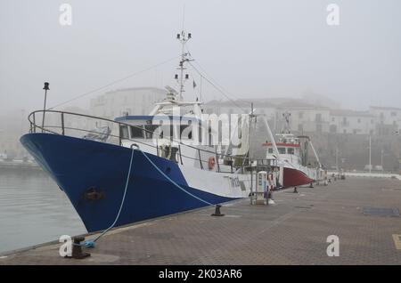 Termoli - Molise - zwei Fischerboote sind im Hafen vertäut, während im Hintergrund der Nebel das alte Dorf umgibt. Stockfoto