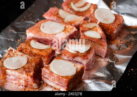 Rohe Schweineribs mit rohen Zwiebeln liegen auf Folie, fertig zum Backen im Ofen. Stockfoto