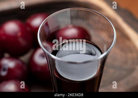 Pflaumenroter Wein auf dunklem Holzhintergrund. Glas mit Rotwein aus nächster Nähe. Stockfoto