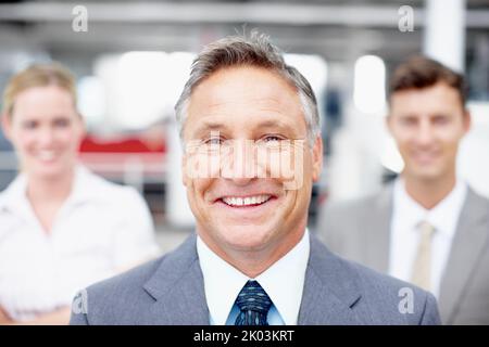 Sie zum Erfolg führen. Porträt einer erfahrenen Führungskraft mit seinen Kollegen, die hinter ihm stehen. Stockfoto