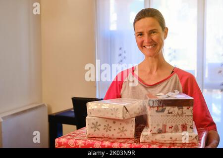 Lächelnde Frau hält Kisten mit einem Weihnachtsgeschenk in ihren Händen Stockfoto