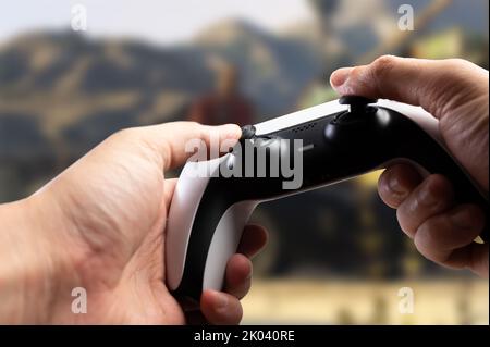 Ein modernes Gamepad GAM22ICB in den Händen eines Spielers vor dem Hintergrund eines Videospiels auf dem Bildschirm eines großen Plasmafernsehers. Cyberspace, virtuelle Realität Stockfoto