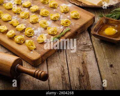 Appetitliche hausgemachte Knödel mit Fleischfüllung werden auf einem hölzernen Schneidebrett auf einem hölzernen Hintergrund ausgelegt. Kochvorgang. Es sind keine Personen drin Stockfoto