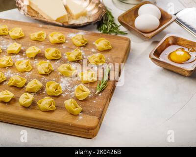 Auf weißem Hintergrund, rohe hausgemachte Knödel auf einem hölzernen Schneidebrett mit einem Zweig Rosmarin. Zutaten, Küchenutensilien. Kochen hausgemachte Müllkippe Stockfoto