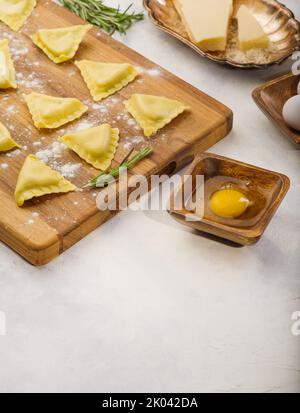 Rohe hausgemachte Ravioli auf einem Holzschneidebrett. Zutaten auf weißem Hintergrund. Italienische Küche. Hausrezepte. Buch mit Rezepten. Es gibt Fr. Stockfoto