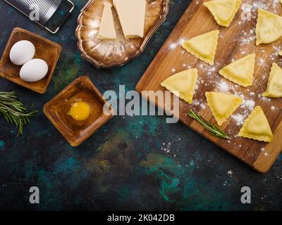 Italienische hausgemachte Ravioli auf einem Holzbrett, Küchenutensilien und Zutaten auf Marmorboden. High-Angle-Ansicht. Es gibt keine Personen in t Stockfoto