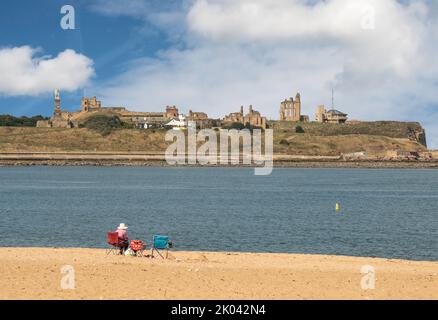 Eine Person sitzt am Littlehaven Beach, South Shields, und blickt über den Fluss Tyne nach Tynemouth Priory and Castle, England, Großbritannien Stockfoto