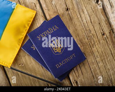 Zwei biometrische ukrainische Pässe und eine kleine Flagge der Ukraine auf einem hölzernen Hintergrund. Persönliche Identifikation, Auslandsreisen, Auswanderung, Flucht aus Stockfoto