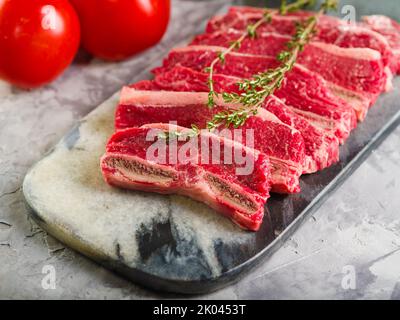 Rohe Fleischstücke mit einem Zweig Rosmarin und reifen Tomaten. Hintergrund der Speisen. Nahaufnahme. Auf dem Foto befinden sich keine Personen. Kochen Fleisch Steaks, goula Stockfoto