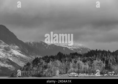 Schwarz-Weiß wunderschöner Blick auf die Winterlandschaft entlang des Loch Leven in Richtung schneebedeckter Berge in der Ferne mit dramatischem Himmel Stockfoto