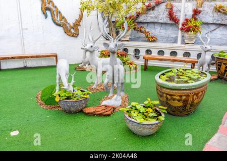 Kleine Hirsch-Statuen mit weißer Farbe auf grünem Boden platziert. Wasserlilie im Topf. Stockfoto