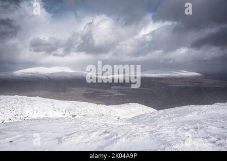 Wunderschöne Winterlandschaft von der Bergspitze in den schottischen Highlands hinunter in Richtung Rannoch Moor während Schneesturm und Spindrift von der Bergspitze hinein Stockfoto