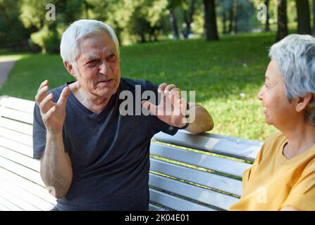 Paare mittleren Alters, multiethnische Ehepartner sitzen auf der Bank Genießen Sie Gespräche im öffentlichen Sommerpark, während Sie freundliche Gespräche führen und dabei Gedanken oder Nachrichten teilen Stockfoto