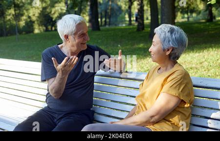 Ältere Paar multiethnischen Ehegatten sitzen Ruhe auf der Bank Genießen Sie Gespräche im öffentlichen Sommerpark mit freundlichen Gespräch teilen Gedanken oder Nachrichten während meeti Stockfoto