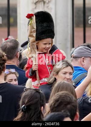 © Jeff Moore Ein junges Mädchen, das als Wache gekleidet ist, sitzt auf den Schultern ihrer Mutter, während sie der verstorbenen Königin Elizabeth II. Vor Buckingham P ihren Respekt zollt Stockfoto