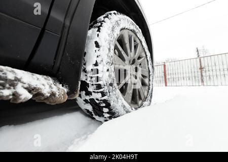 Schneebedecktes Rad eines SUV-Autos, das an einem Wintertag in einer Schneeverwehung steht Stockfoto