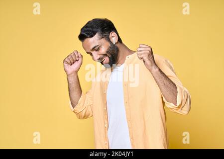 Glücklicher indischer Mann, der in Ohrhörern tanzt und Musik auf Gelb hört. Stockfoto