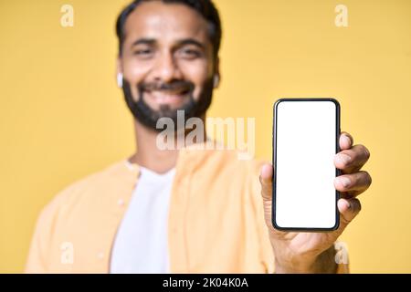 Glücklicher indischer Mann zeigt Handy-Mockup-Bildschirm isoliert auf gelb. Stockfoto