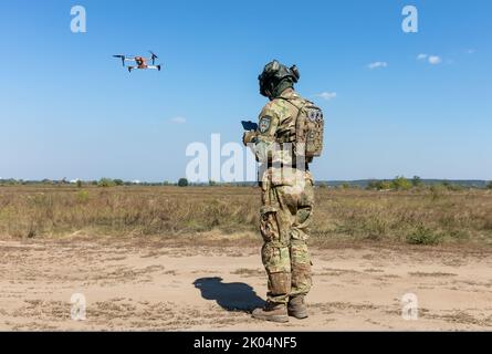 Ein Drohnenbetreiber startet einen Quadcopter, um den Betrieb eines Evakuierungsroboters während seiner Feldtests zu überwachen. Feldtests der Multizweck-Crawler-Drohne Themis der estnischen Firma Milrem Robotics, die vom medizinischen Bataillon „Hospitalers“ für Evakuierungszwecke an der Front verwundete Soldaten eingesetzt werden soll. Der Evakuierungsroboter „Zhuravel“ bestand den ersten Test. Der Roboter wird an vorderster Front eingesetzt, an Orten, an denen es für Mediziner schwierig ist, mit dem Fahrzeug oder zu Fuß zu erreichen. Stockfoto