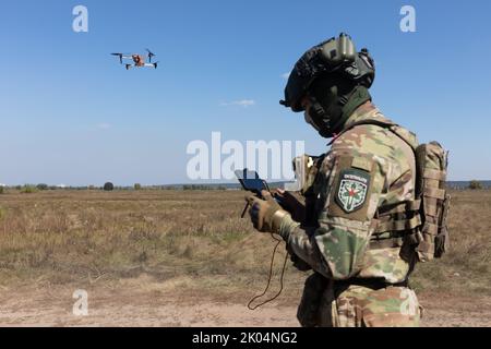 Ein Drohnenbetreiber startet einen Quadcopter, um den Betrieb eines Evakuierungsroboters während seiner Feldtests zu überwachen. Feldtests der Multizweck-Crawler-Drohne Themis der estnischen Firma Milrem Robotics, die vom medizinischen Bataillon „Hospitalers“ für Evakuierungszwecke an der Front verwundete Soldaten eingesetzt werden soll. Der Evakuierungsroboter „Zhuravel“ bestand den ersten Test. Der Roboter wird an vorderster Front eingesetzt, an Orten, an denen es für Mediziner schwierig ist, mit dem Fahrzeug oder zu Fuß zu erreichen. Stockfoto