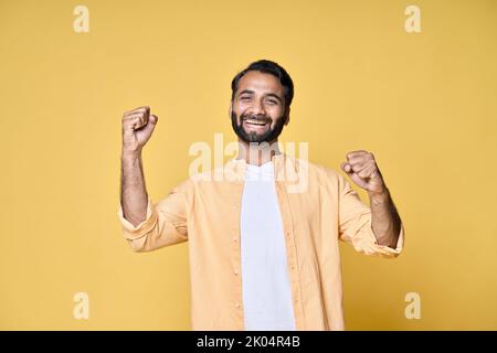 Fröhlicher, fröhlicher indischer Mann, der auf gelbem Hintergrund die Fäuste hebt. Stockfoto