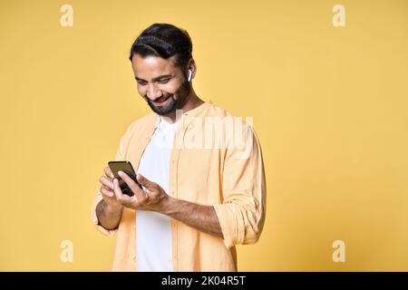 Indischer Mann trägt Ohrstöpsel mit Mobiltelefon isoliert gelben Hintergrund. Stockfoto