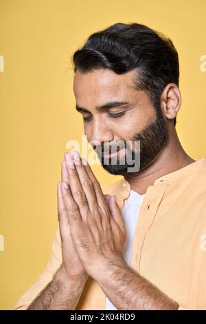 Achtsamer indischer Mann meditiert und hält Hände in namaste isoliert auf Gelb. Stockfoto