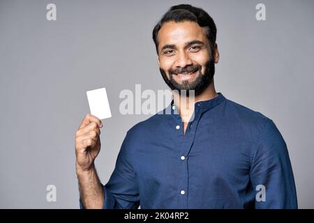 Lächelnder indischer Geschäftsmann, der die Kreditkarte auf grauem Hintergrund isoliert hält. Stockfoto
