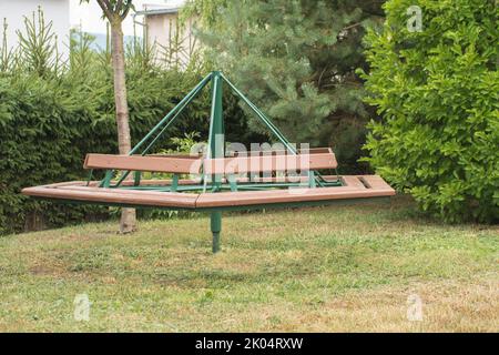 Retro-sozialistisches Kinderkarussell aus Holz und Eisen. Kinderroundabout im Hinterhof platziert. Umgeben von Gartenbelaubung. Hergestellt in der Tschechoslowakei. Stockfoto