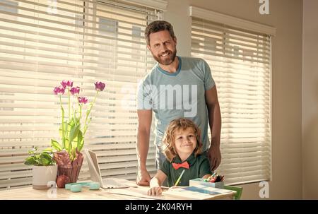 Glücklicher bärtiger Vater, der Schulaufgaben mit seinem Sohn im Klassenzimmer, zu Hause, geschrieben hat Stockfoto