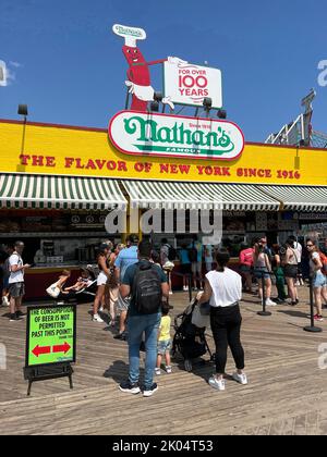 Leute, die sich für Hot Dogs im berühmten Nathan's on the Boardwalk auf Coney Island am Strand in Brooklyn, New York, anstellen. Stockfoto