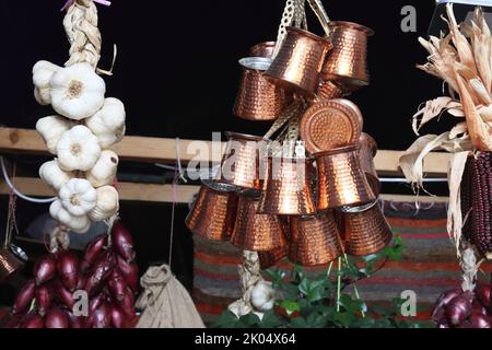 Ein Haufen türkisch geprägter cooper-Bronze-Kaffeekannen und Zöpfe mit weißem Knoblauch und roten Zwiebeln hängen auf dem orientalischen Marktplatz in Heildeberg. Clo Stockfoto