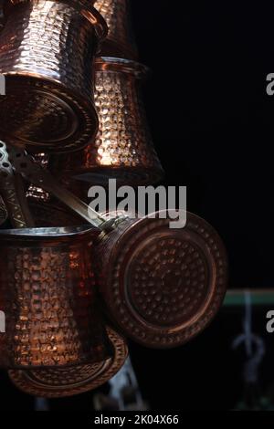 Ein Haufen türkisch geprägter cooper-Bronze-Kaffeekannen hängt auf dem orientalischen Marktplatz in Heildeberg. Schließenbild, Seitenansicht. Schwarzer Hintergrund. Spa Kopieren Stockfoto