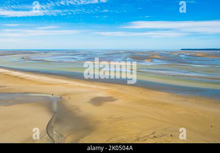 Touristen, die bei Ebbe auf den farbenfrohen Sandflächen rund um den Mont Saint Michel, die Normandie und Nordfrankreich wandern Stockfoto