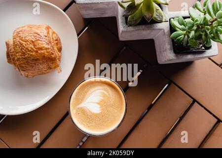 Tasse flaches weißes und Schokoladencroissant auf dem Tisch im modernen Café, Draufsicht Stockfoto