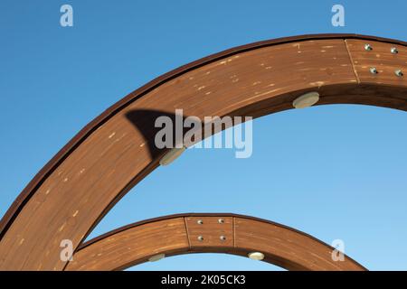 Holzbogen gegen den Himmel. Architekturdetails. Stützstruktur. Lichtbogen im Gebäude. Stockfoto