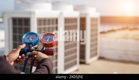 Luftreparaturmechaniker mit Messgeräten zum Befüllen von industriellen Klimaanlagen und zur Überprüfung der Wartung der Außenluftkompressoreinheit. Stockfoto