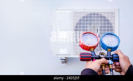 Luftreparaturmechaniker mit Messgeräten zum Befüllen von industriellen Klimaanlagen und zur Überprüfung der Wartung der Außenluftkompressoreinheit. Stockfoto